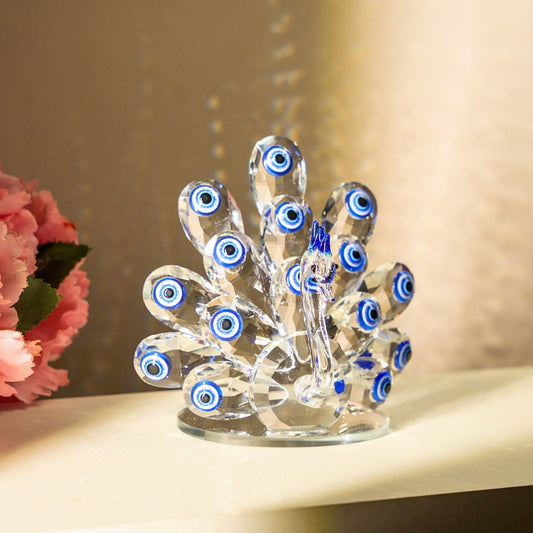 Decorative glass peacock with evil eye design on a shelf with flowers.