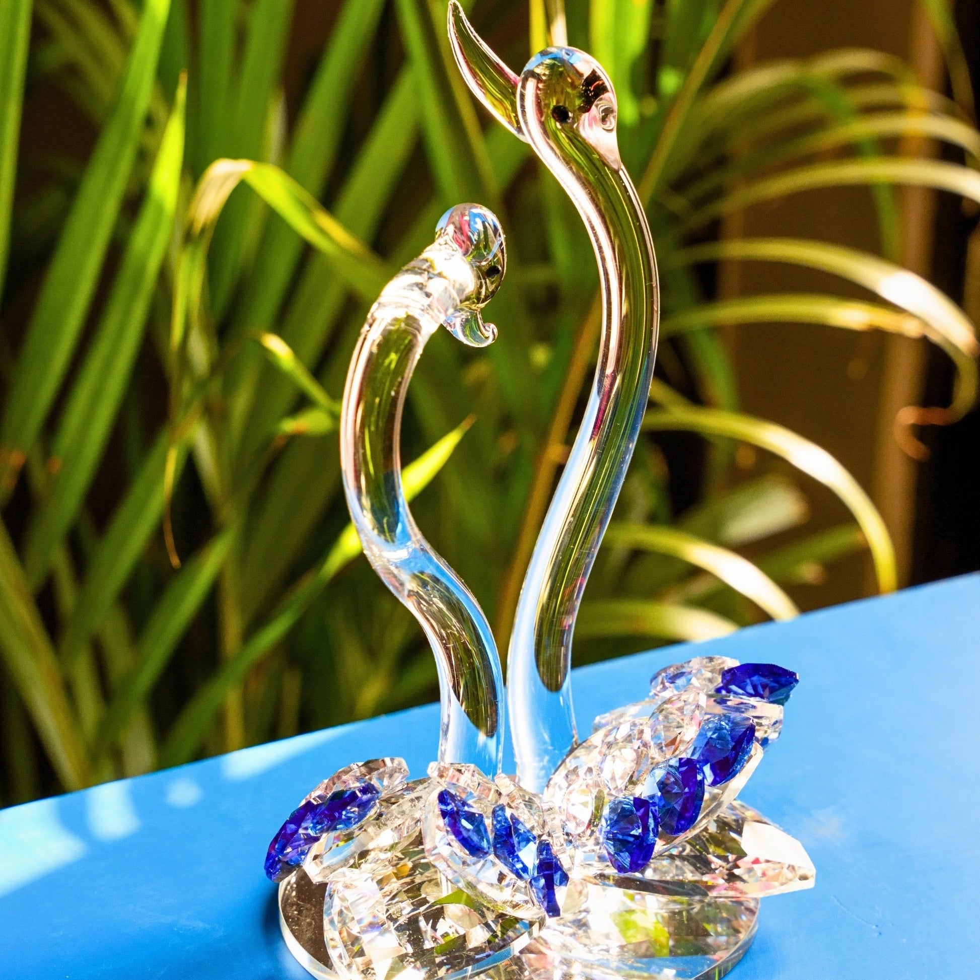 Crystal swan figurine on a reflective surface with green foliage in the background
