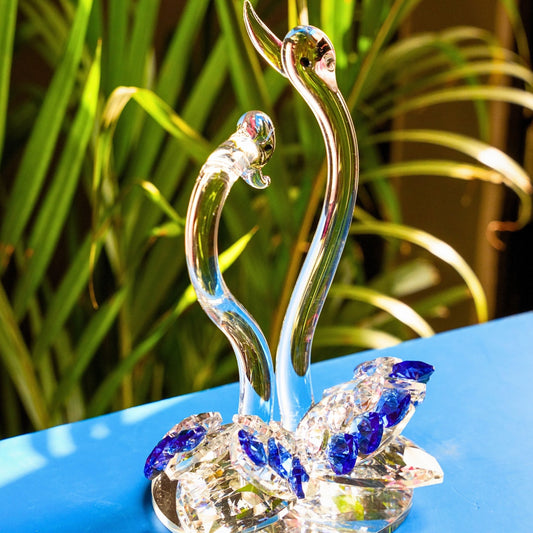 Crystal swan figurine on a reflective surface with green foliage in the background
