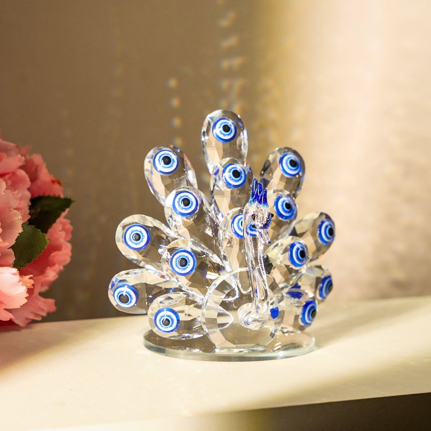Decorative glass peacock with evil eye design on a shelf with flowers.